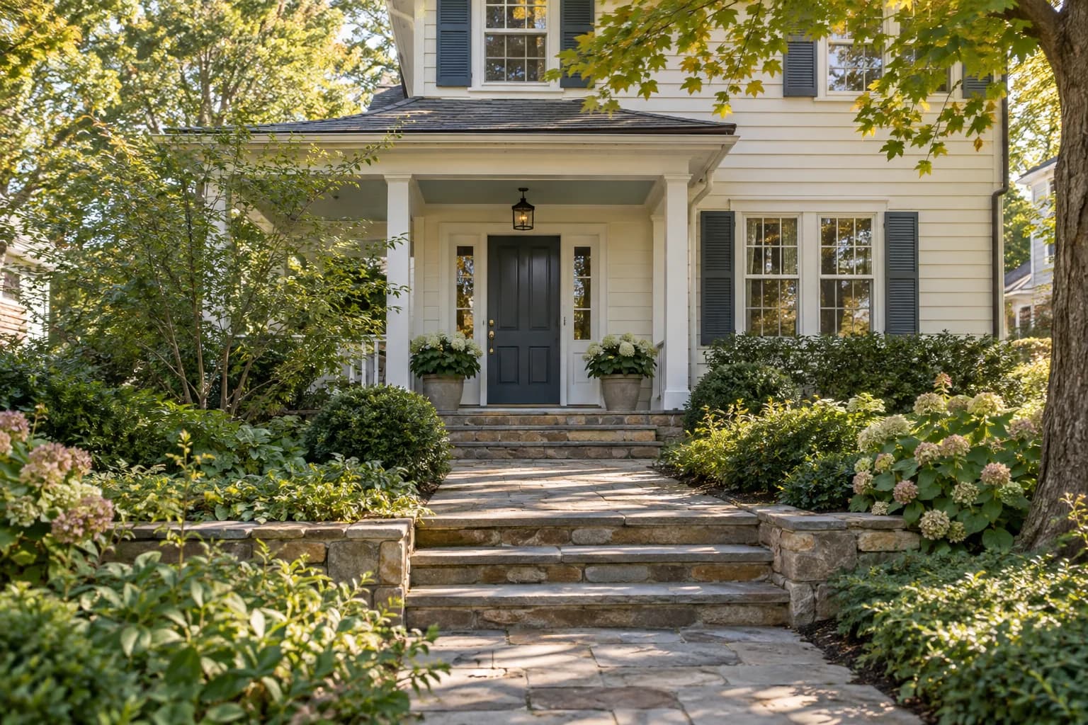 A cream clapboard home with a slate blue front door, stone path and landscaped trees